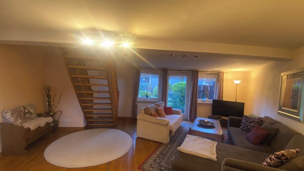 Ein Wohnzimmer mit Treppe, einer Couch, einem Fernseher und einem großen Fenster.