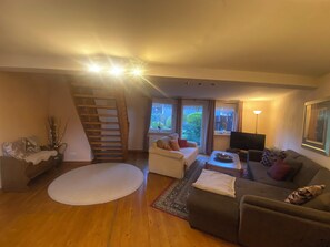 A living room with a staircase, a sofa, a TV, and a large window. - 5 bedrooms, quiet town location, garden, 2 parking spaces, 200m to market square (Goslar)