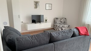 Ein modernes Wohnzimmer mit einem grauen Sofa, einer weißen Unterhaltungsecke mit Flachbildfernseher und einem gemusterten Sessel.