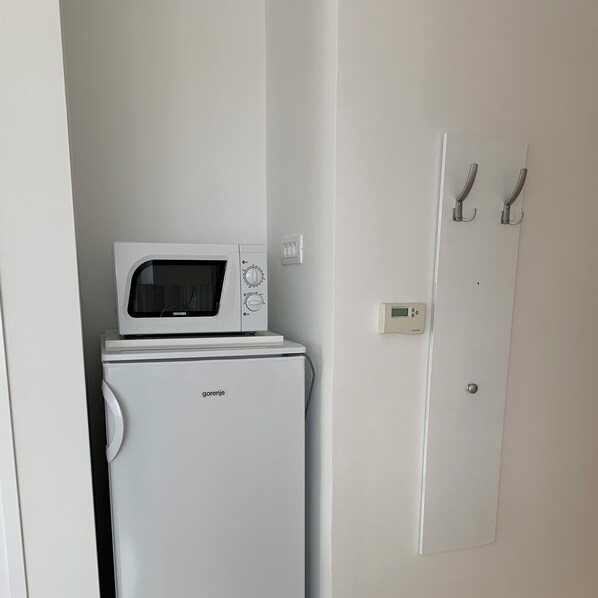A compact room with a white washing machine and a microwave on top. There is a door with a handle and a wall-mounted thermostat.