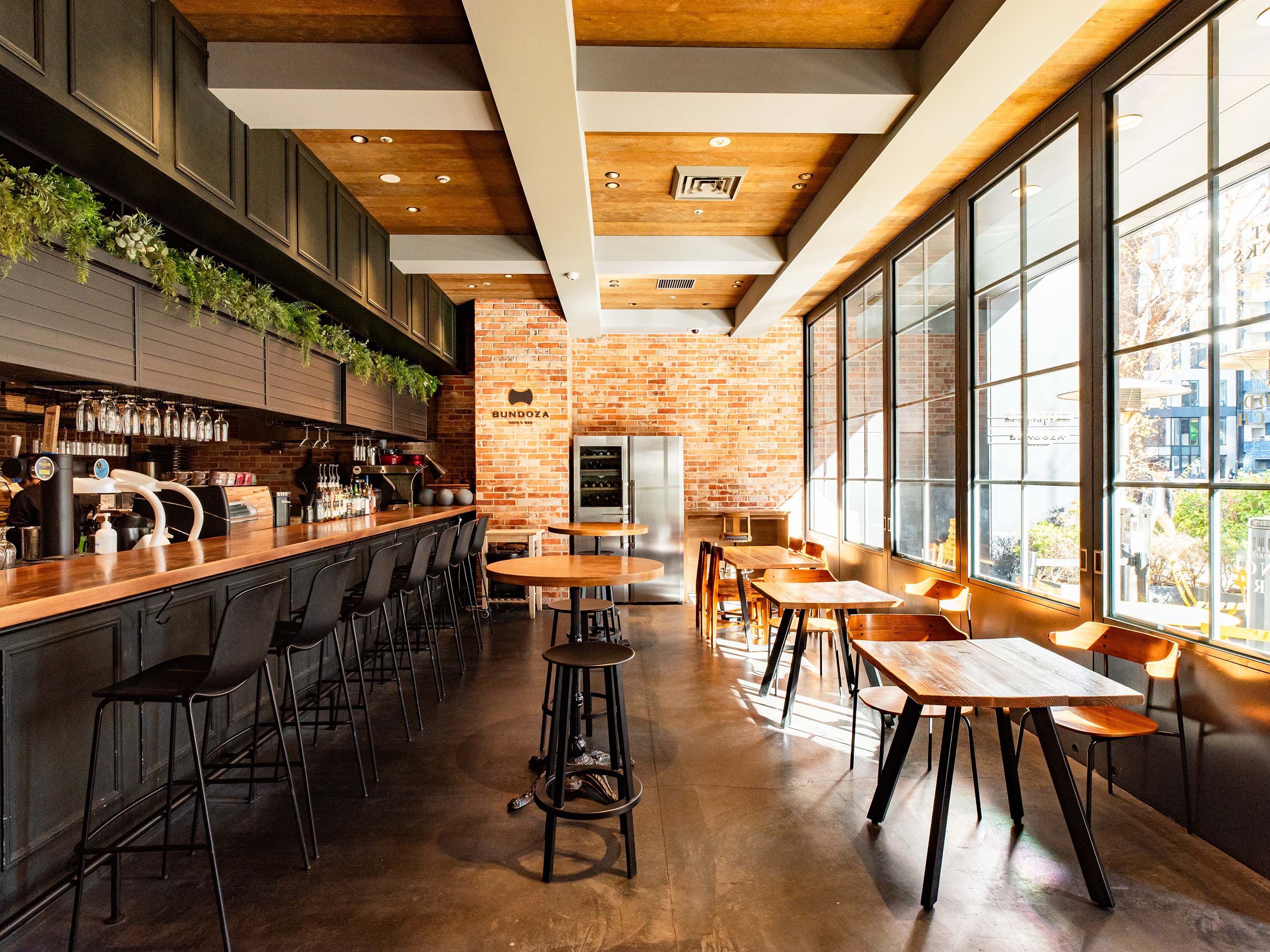 A modern bar with a brick wall, wooden ceiling, and large windows.