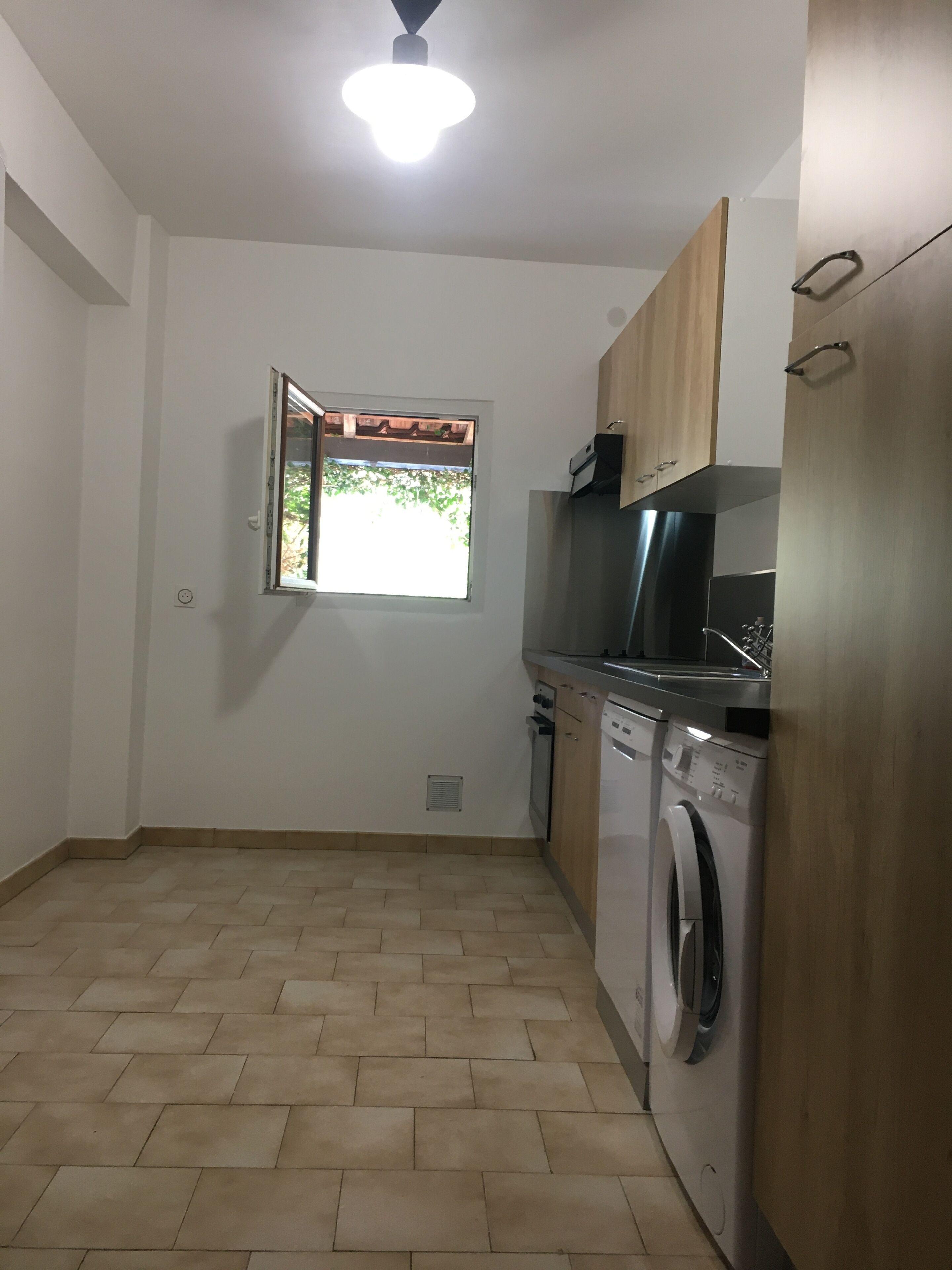 A compact kitchen with a washing machine, a stove, and a window with a view of greenery.