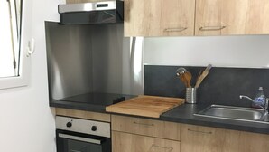 A modern kitchen with wooden cabinets, a stainless steel range hood, a built-in oven, and a black countertop. - rent large calm F1 at the door of the center town of Ajaccio (Sarrola-Carcopino)