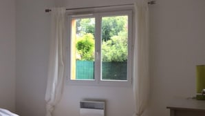 Un dormitorio con cama, radiador, ventana con cortinas y ventilador de techo.