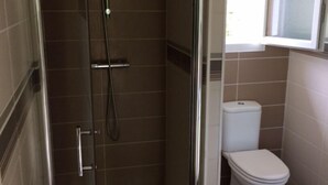 Un baño con ducha envuelta en vidrio, un inodoro y un ventanal.