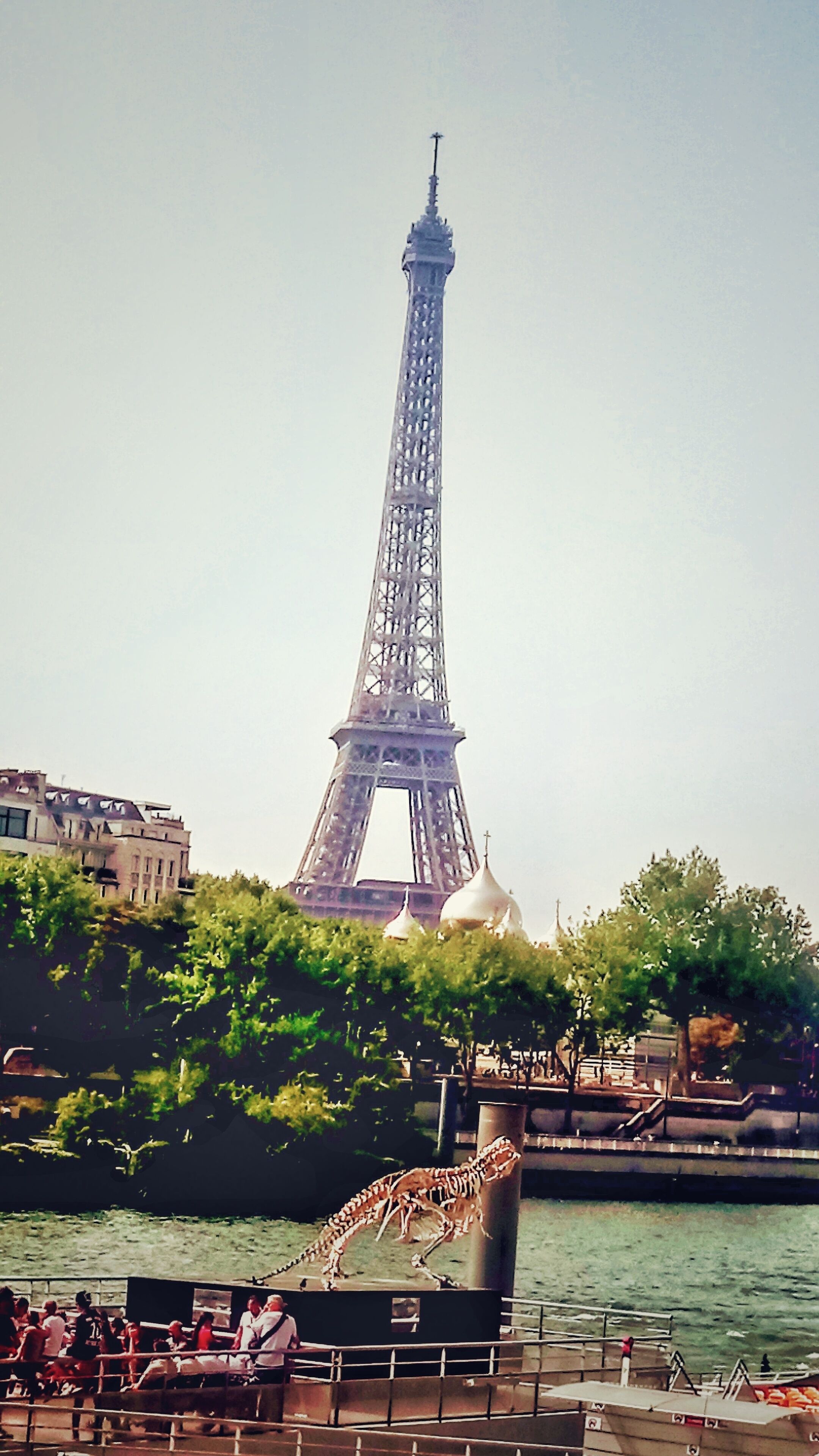 A Torre Eiffel com um rio em primeiro plano e um barco com pessoas.