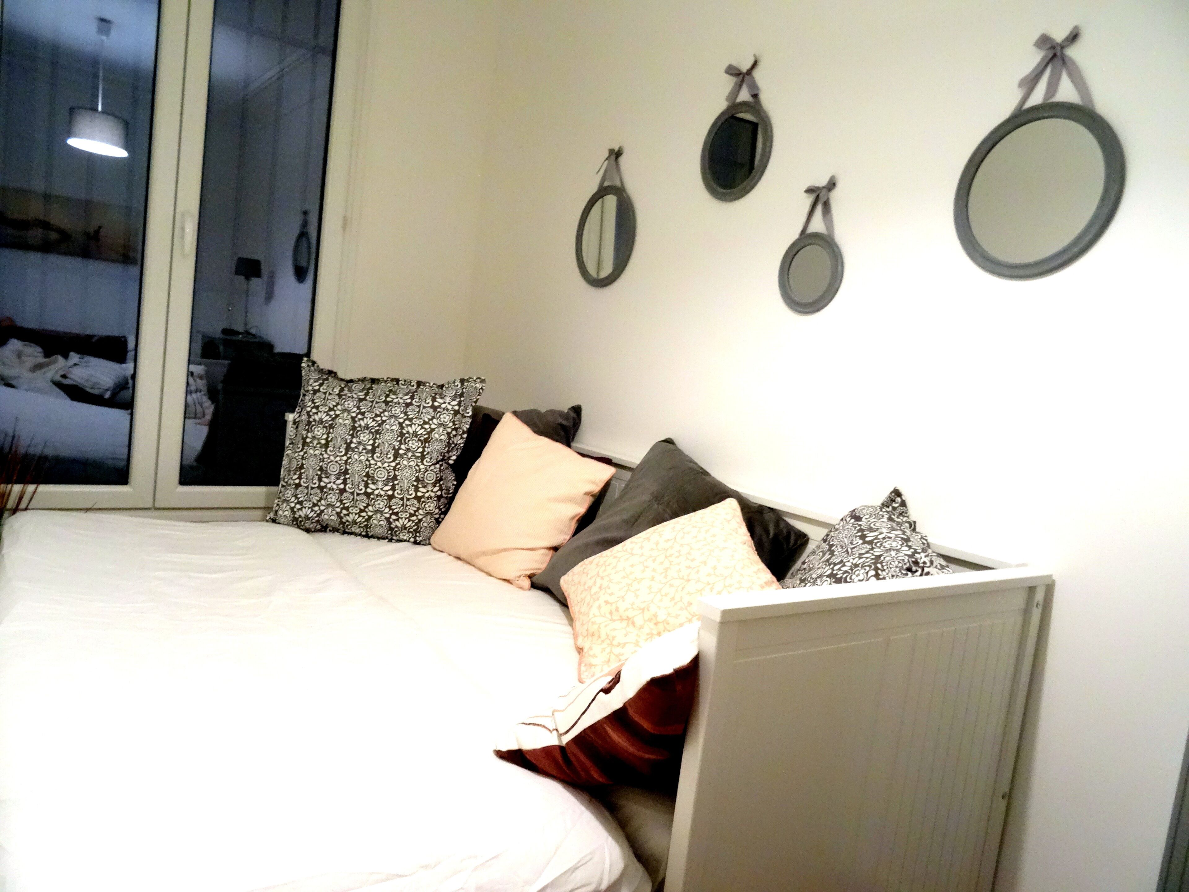 A bedroom with a bed, pillows, and three wall-mounted mirrors.