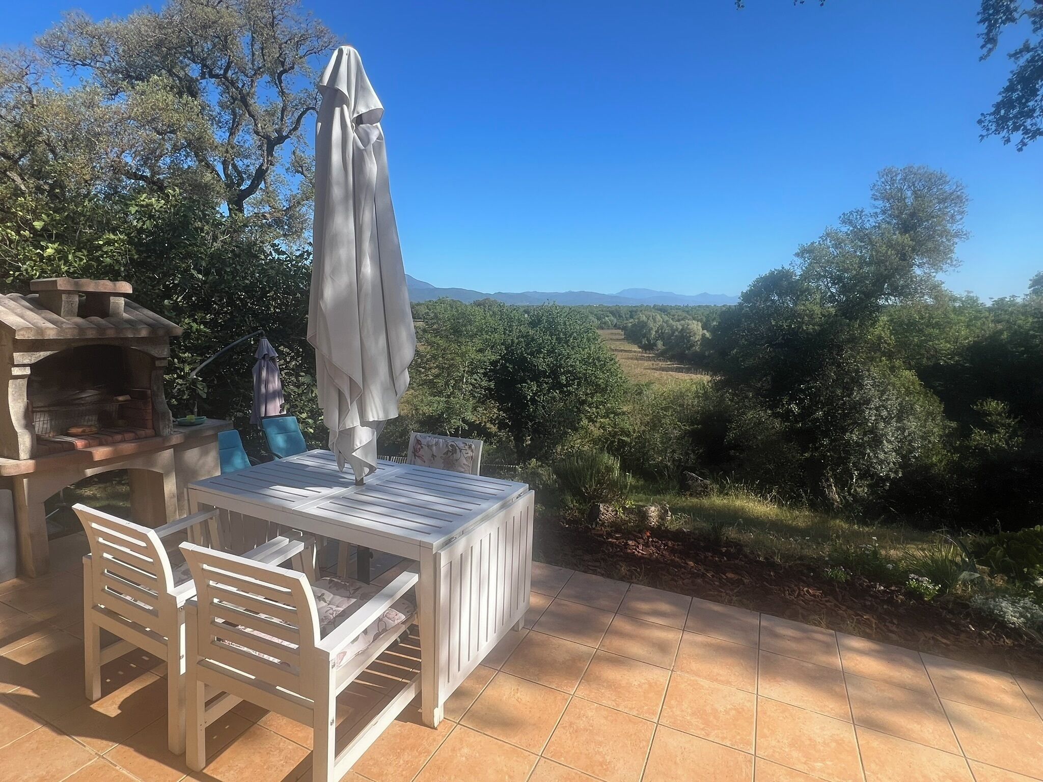 An outdoor patio with a stone oven, white furniture, and a view of a vineyard.