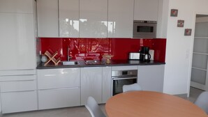 Une cuisine moderne avec des meubles blancs, un pare-feu rouge, un four encastré et une table à manger avec des chaises.