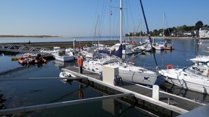 Un port de plaisance où sont amarrés différents types de bateaux, un ciel dégagé et une étendue d’eau calme.