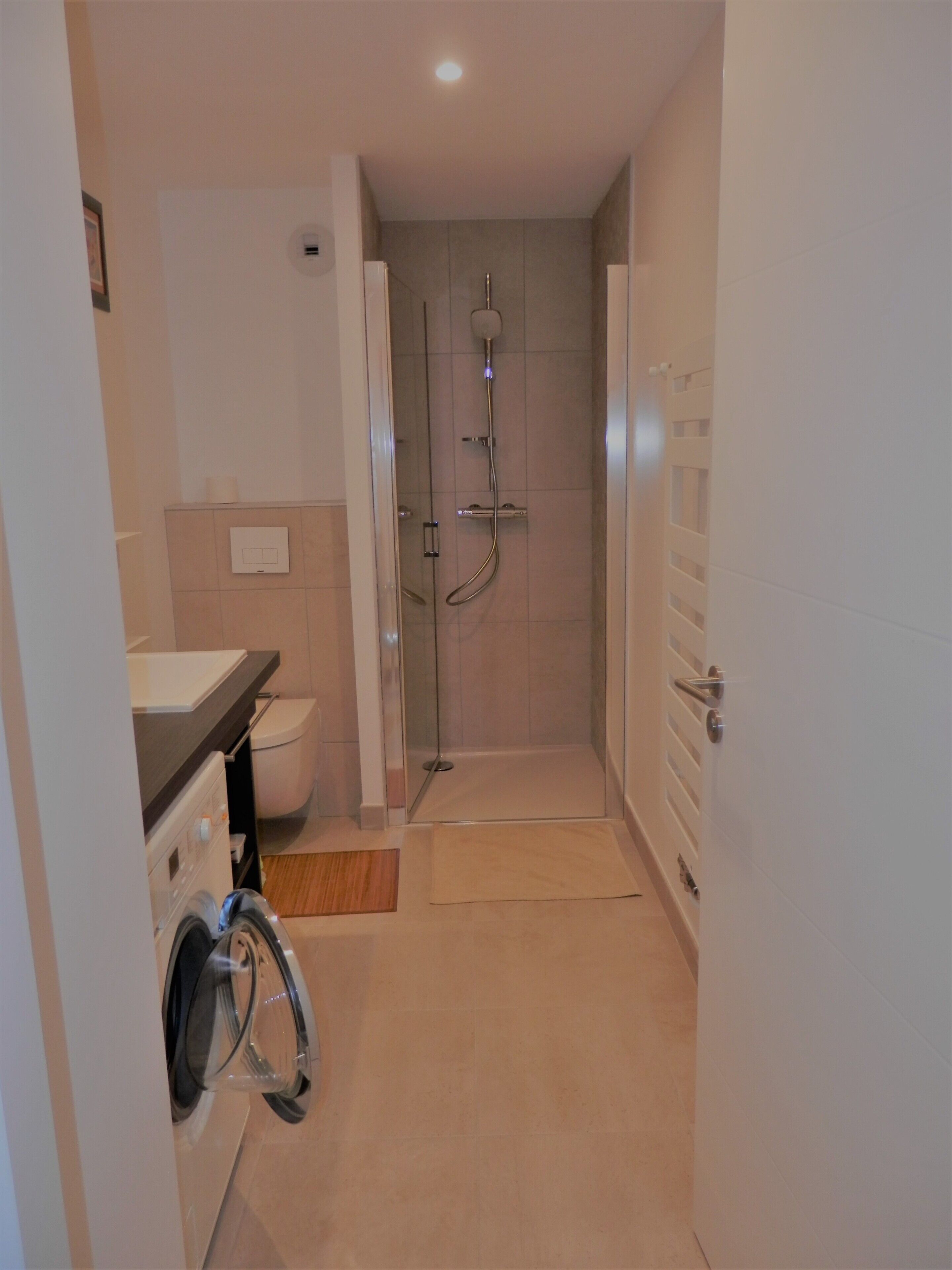Une salle de bain moderne équipée d’une douche, de toilettes et d’un lave-linge.