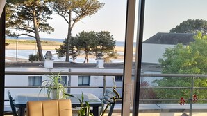 Un balcon avec une table et des chaises, des plantes en pot et une vue sur la plage et l’océan.