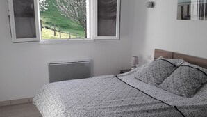 A bedroom with a bed, a window, a bedside table, and a wall-mounted light.