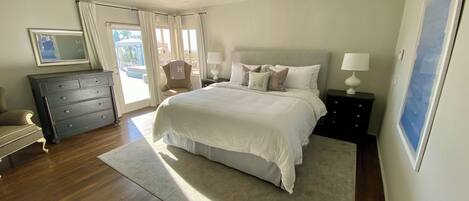 A bedroom with a large bed, a dresser, a chair, and a desk with a lamp.