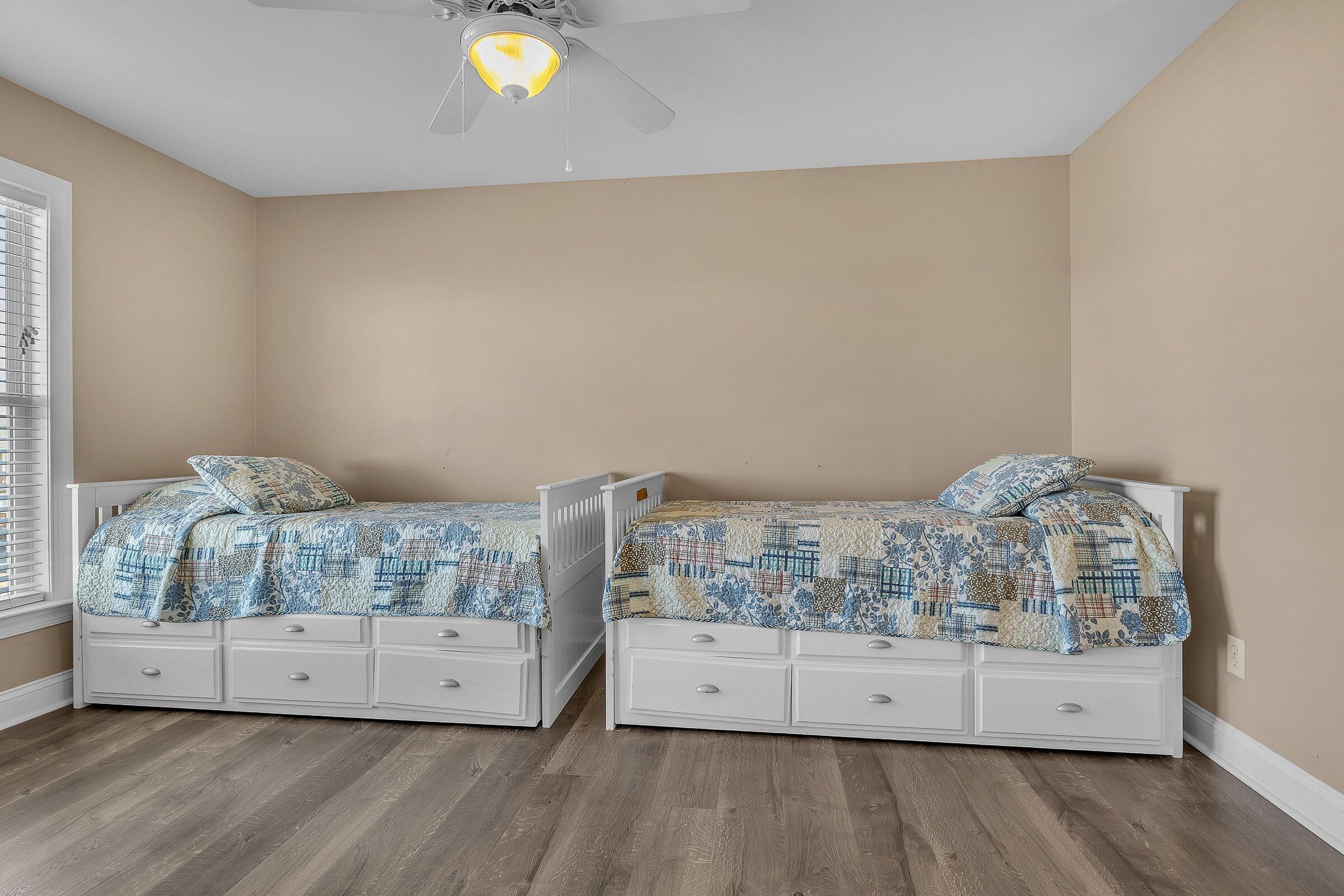 Un dormitorio con dos camas blancas, cada una con una colcha y almohadas estampadas, y un ventilador de techo.
