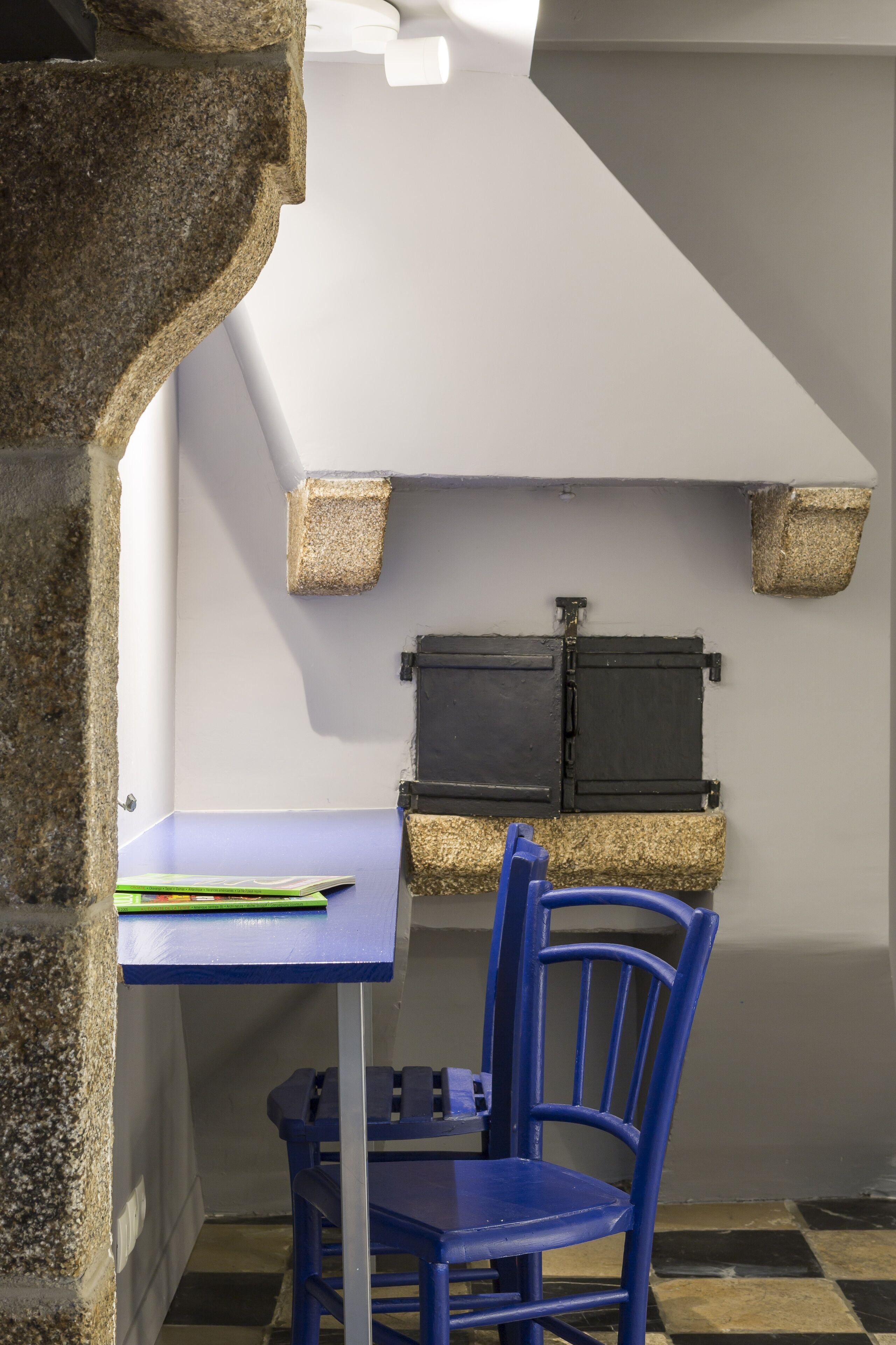 Une petite cuisine avec une table et une chaise bleues, des murs en pierre et un meuble noir.