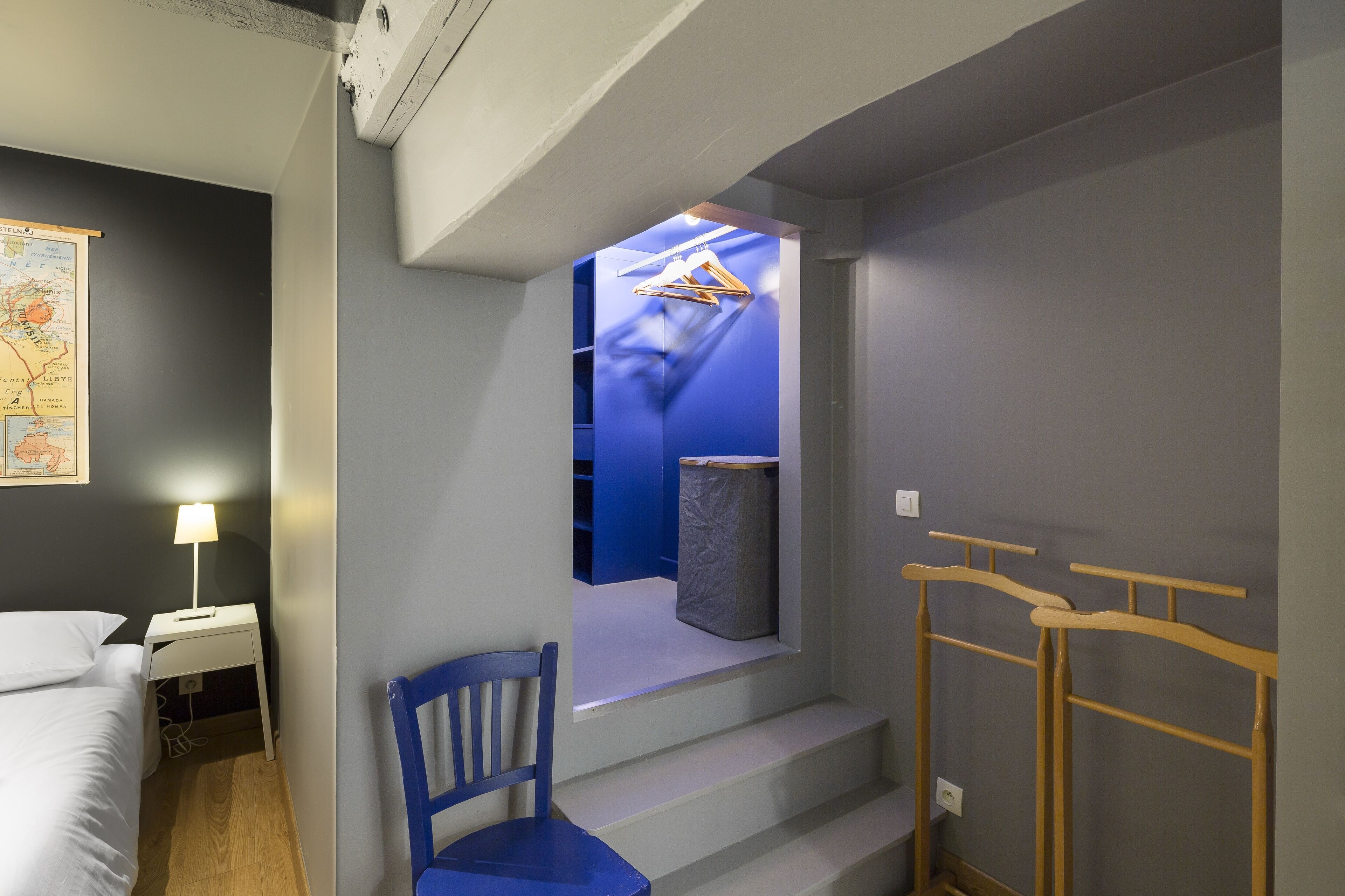 A hotel room with a bed, a desk with a lamp, a chair, and a staircase leading to a bathroom.