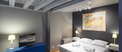 A modern bedroom with a large bed, a flat-screen TV, a map on the wall, and a blue dresser.