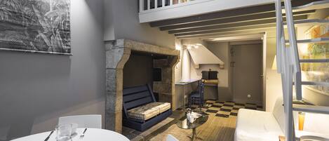 Une pièce chaleureuse avec un sol à carreaux, un canapé doté d’une banquette intégrée, une table à manger mise avec des assiettes et des verres, et un escalier menant à un niveau supérieur.