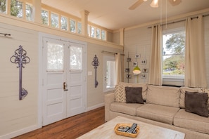 Relax in this spacious living room with a high ceiling and large windows, featuring a comfortable sofa and a wooden coffee table.