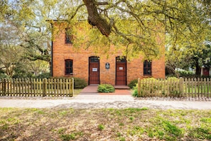 Traditional architecture with a central entrance, flanked by windows with iron bars, set amidst a well-manicured lawn and lush greenery.