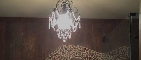 Une salle de bain avec un mur en bois, une arche ornée d’une mosaïque de pierres, un porte-serviettes avec des serviettes et un lustre.