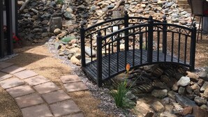 Un jardín con un sendero de piedra que lleva a una terraza de madera, rodeado por una cerca y una pérgola de madera.
