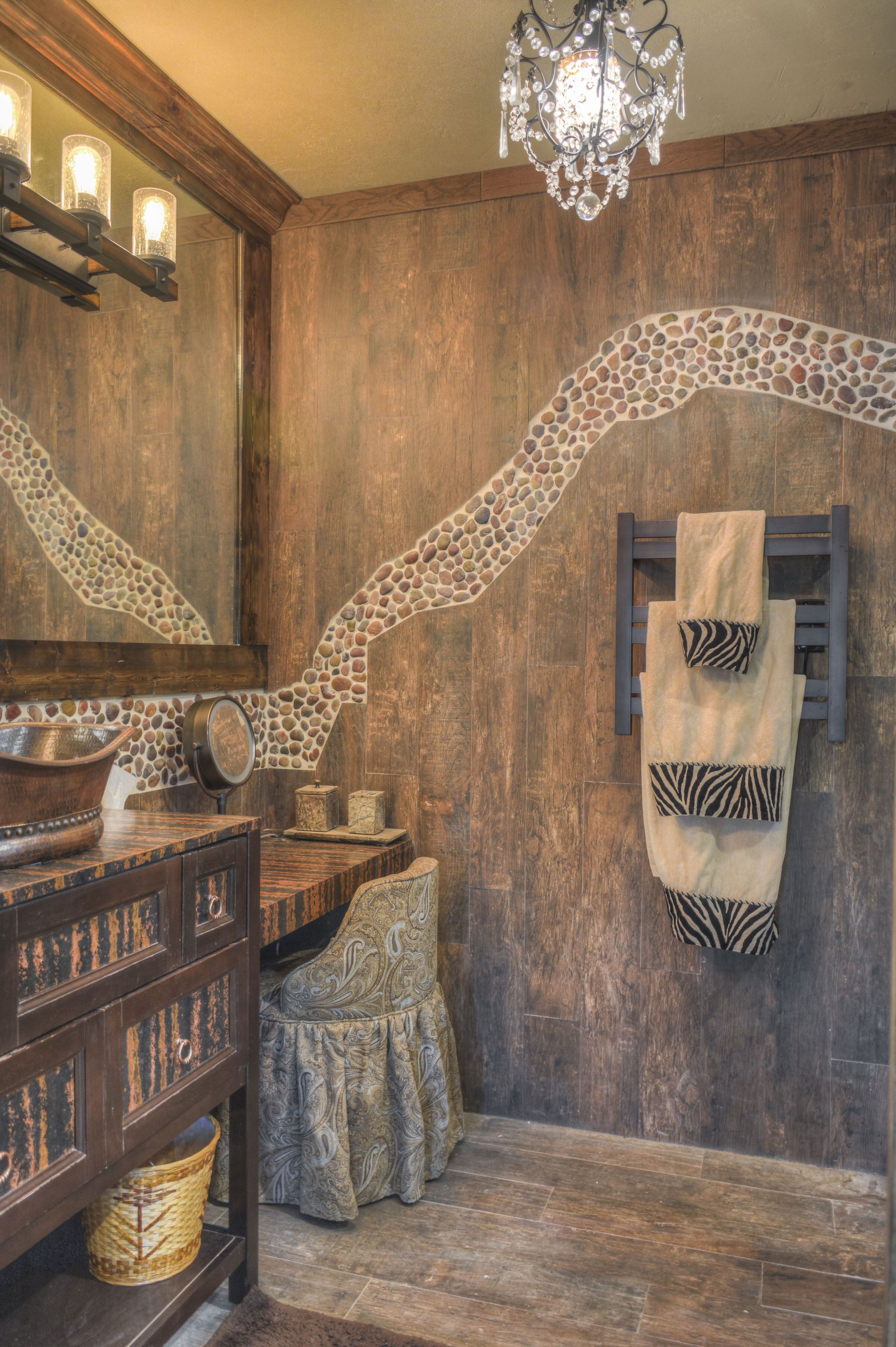 Un baño rústico con paredes de madera, un arco de mosaico de piedra, una araña y un perchero con toallas de estampado de cebra.