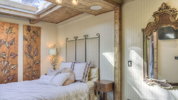 Un dormitorio con una cama, una mesita de noche, un espejo y un cuadro floral en la pared.