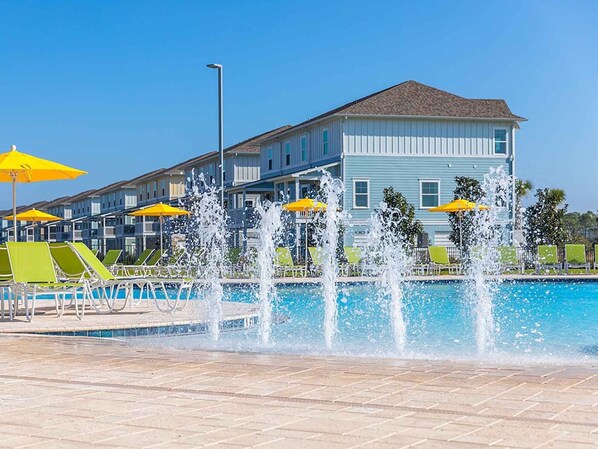 Una piscina con getti d'acqua multipli, circondata da poltroncine verdi e ombrelloni gialli.