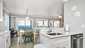 A modern kitchen with white cabinetry, a marble countertop, and a view of the ocean through large windows. - Dip Inn: Basic beach house with upgraded appliances (Oak Island)