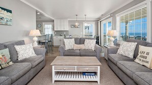 A modern living room with grey sofas, a wooden coffee table, and a view of the ocean through large windows. - Dip Inn: Basic beach house with upgraded appliances (Oak Island)