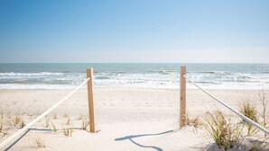 A sandy beach with a rope barrier and wooden posts, leading to the ocean. - Dip Inn: Basic beach house with upgraded appliances (Oak Island)