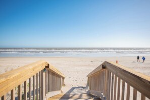 A wooden boardwalk leading to a beach with two people walking.