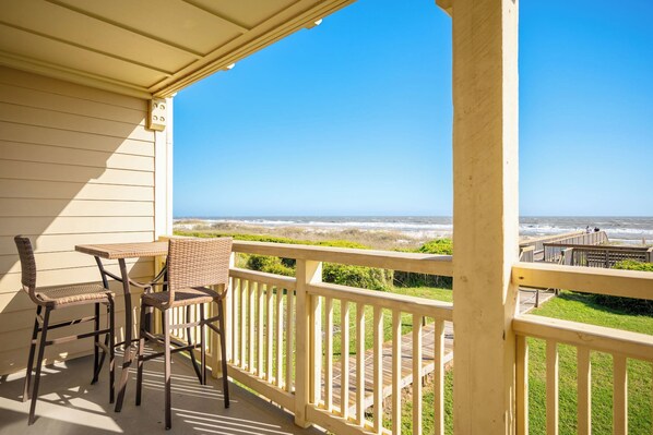 A covered outdoor area with a table and chairs, overlooking a beach with a wooden walkway.