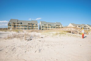 Un hotel fronte spiaggia con numerosi balconi e una passerella in legno che conduce alla spiaggia.