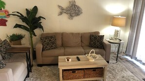 A living room with a beige sofa, a coffee table, a large plant, and decorative wall art. - Beautiful 2-BR Bayside Condo W/Pool, Gull Way Villas, Short Walk To Beach (Ocean City)