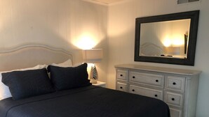 A neatly made bed with a dark bedspread, a white headboard, and two pillows. There is a white dresser with multiple drawers and a mirror above it. - Beautiful 2-BR Bayside Condo W/Pool, Gull Way Villas, Short Walk To Beach (Ocean City)