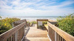 Een houten looppad dat naar een strand leidt, met een strandwachtbord.