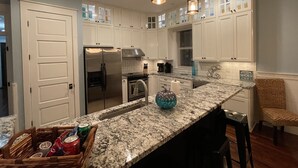 A modern kitchen with white cabinets, a stainless steel refrigerator, granite countertops, and pendant lighting. - NEW FALL RATES! Picturesque Cottage Retreat in Cassine Village, Seagrove Beach (Santa Rosa Beach)