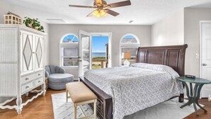 A bedroom with a bed, a bench, a small table, a wardrobe, and a ceiling fan. - Heron Pointe: Oceanwalk home with waterway views and just a short stroll to the (Oak Island)