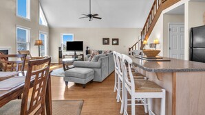 A spacious living area with a dining table, sofa, and kitchen counter. - Heron Pointe: Oceanwalk home with waterway views and just a short stroll to the (Oak Island)