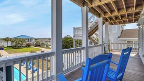 A covered deck with a pool, blue Adirondack chairs, and a view of neighboring houses. - Coast is Clear: Expansive Ocean and Waterway Views w/Private Backyard Pool (Oak Island)
