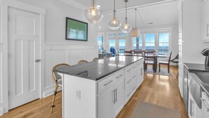 A modern kitchen with a central island, pendant lighting, and a view to the outside. - Coast is Clear: Expansive Ocean and Waterway Views w/Private Backyard Pool (Oak Island)