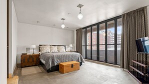 Een moderne slaapkamer met een groot bed, een houten kist, een televisie en een groot raam met gordijnen.