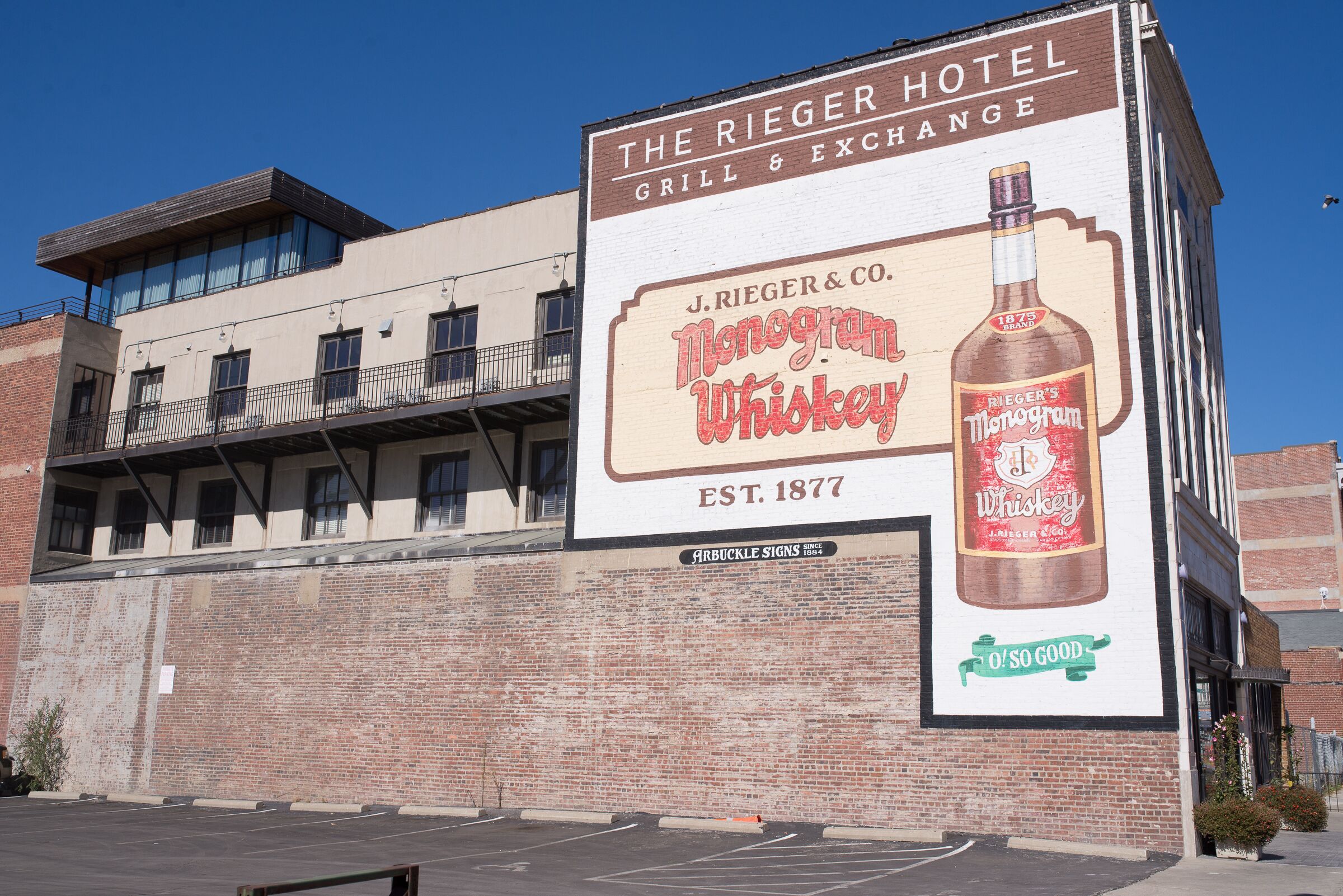 A hotel with a large billboard advertising J. Rieger & Co. Monogram Whiskey.