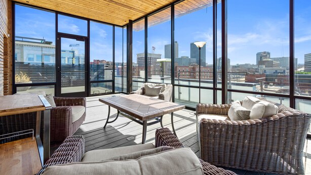 Een ruim balkon met rieten meubels, grote ramen en uitzicht op de stadshemel.