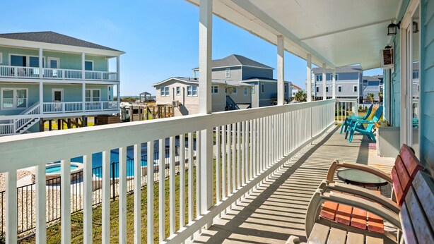 A covered deck with a white railing, outdoor seating, and a view of adjacent houses. - The Hideaway: Dog-friendly Unit in Multiplex Close to Public Beach Access (Oak Island)