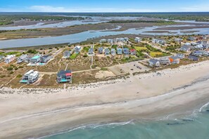Vue aérienne d’une zone résidentielle côtière, avec des maisons, une plage et un paysage marécageux.