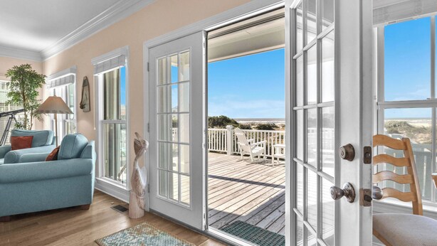 Una habitación con un amplio ventanal corredero que da a una terraza de madera con vista a la playa.